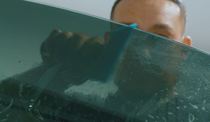 Technician applying window tint film to a car door window using a blue squeegee tool.