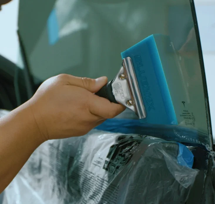 Close-up of a hand using a blue squeegee tool to install window tint film on a car door.