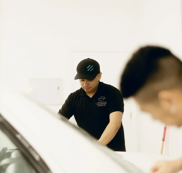 Technician from ArtDeShine Studios carefully applying paint protection film (PPF) in a clean, professional workshop environment.