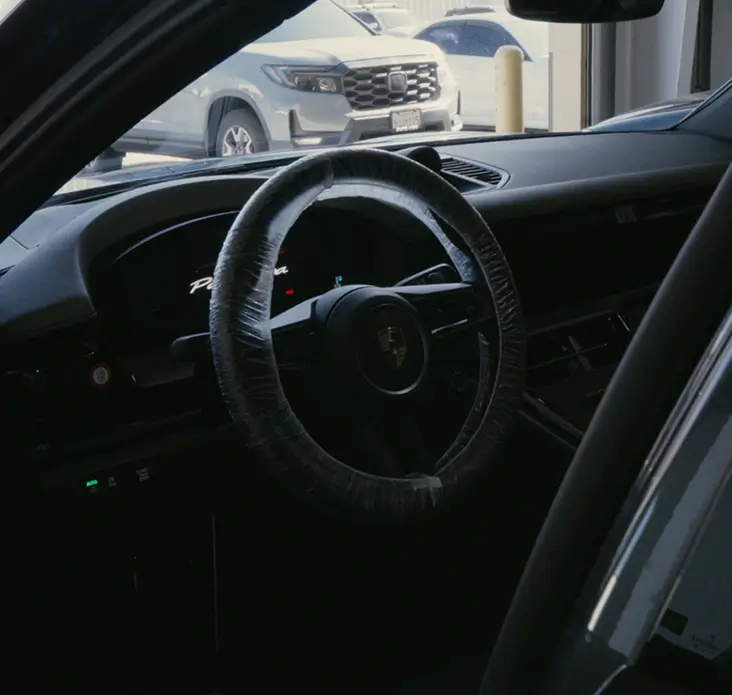 Interior view of a Porsche showing the steering wheel and dashboard, highlighting a vehicle ready for precision PPF installation.